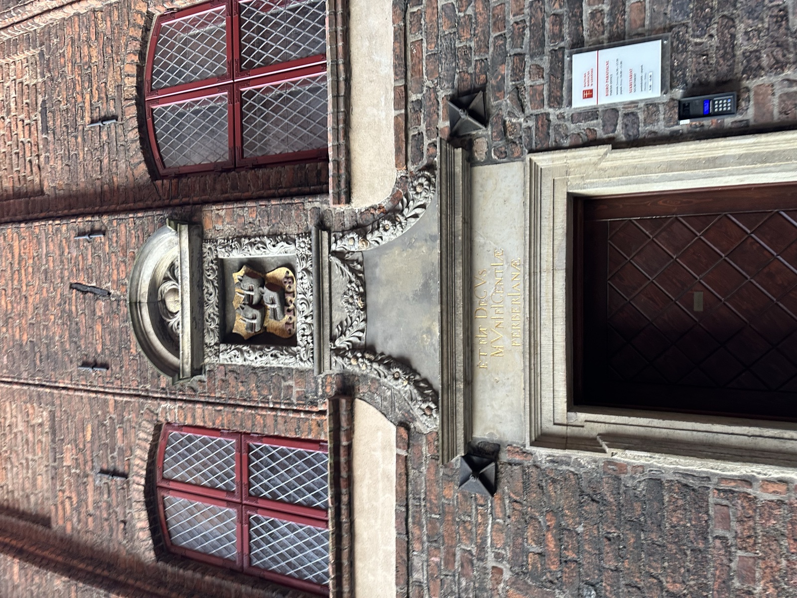 A heraldic keystone carved between two arched, red-trimmed windows of a merchant house